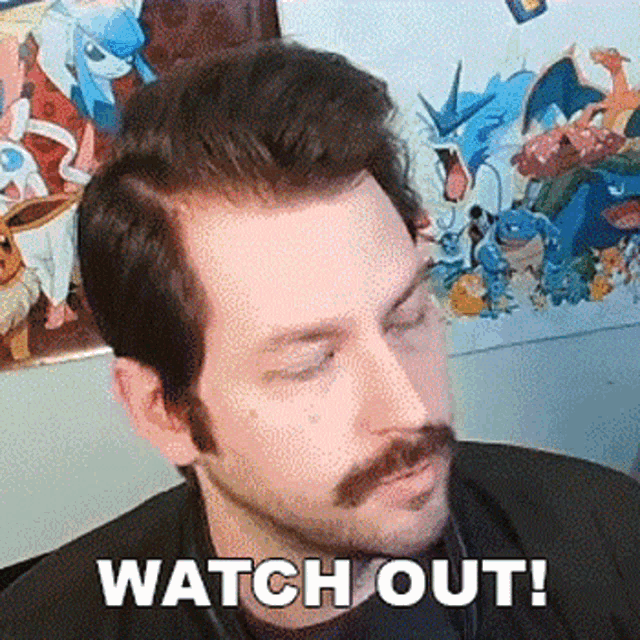 a man with a mustache is sitting in front of a wall with pokemon pictures and the words watch out written on it .