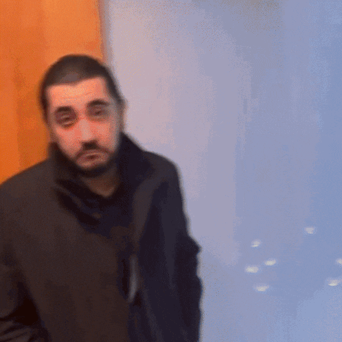 a man with a beard wearing a black coat stands in front of a door