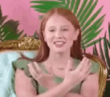 a woman in a green dress is sitting in a chair with her hands folded and smiling .