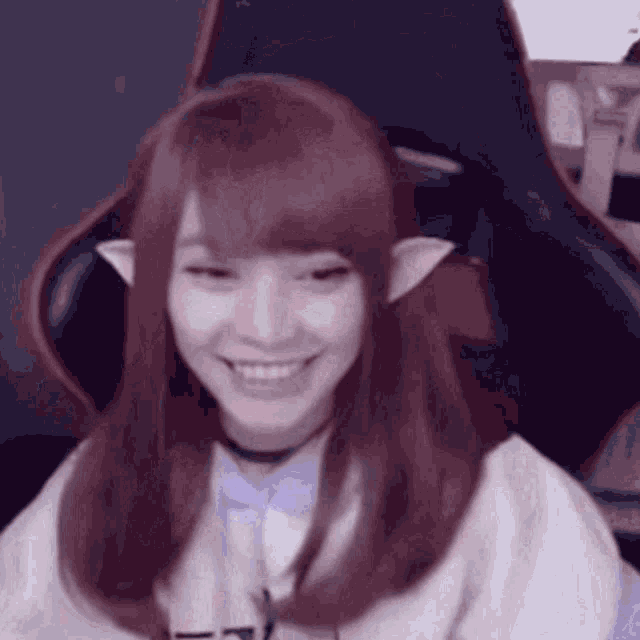 a girl with red hair and elf ears is sitting in a chair and smiling .