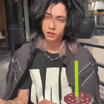 a young man with long hair is wearing a black shirt with the letter m on it