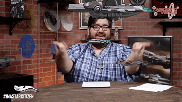 a man in a plaid shirt is sitting at a table with a space ship in the background