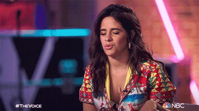 a woman in a colorful shirt is sitting in front of a nbc logo