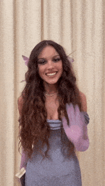 a woman in a purple dress and purple gloves is standing in front of a white curtain .