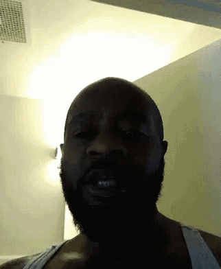 a man with a beard wearing a tank top looks at the camera