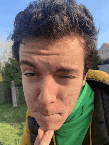 a young man wearing a green sweater and a yellow jacket makes a face