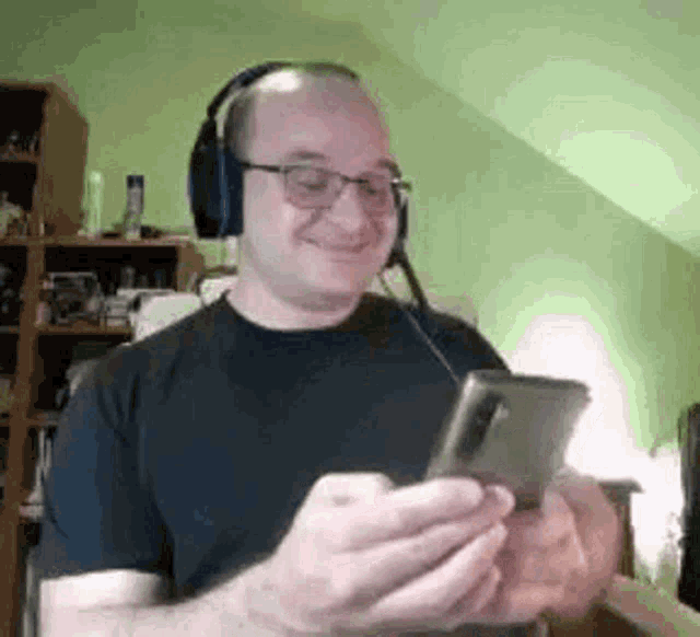 a man wearing headphones and glasses is smiling while looking at his cell phone .