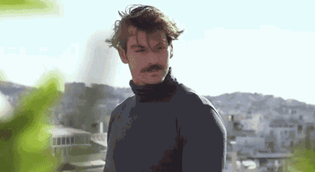 a man with a mustache is wearing a black turtleneck sweater and looking at the camera .