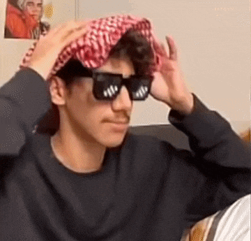 a young man wearing sunglasses and a head scarf is sitting on a couch .