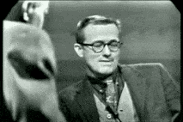 a black and white photo of a man wearing glasses and a suit and tie .