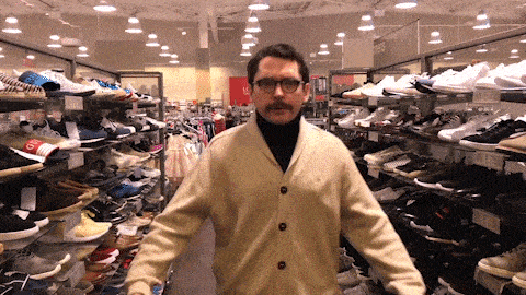 a man with a mustache and glasses is standing in a shoe store with a sign that says ' 876 ' on it