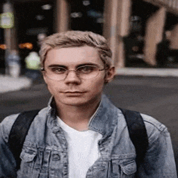 a young man wearing glasses and a denim jacket is walking down a street .