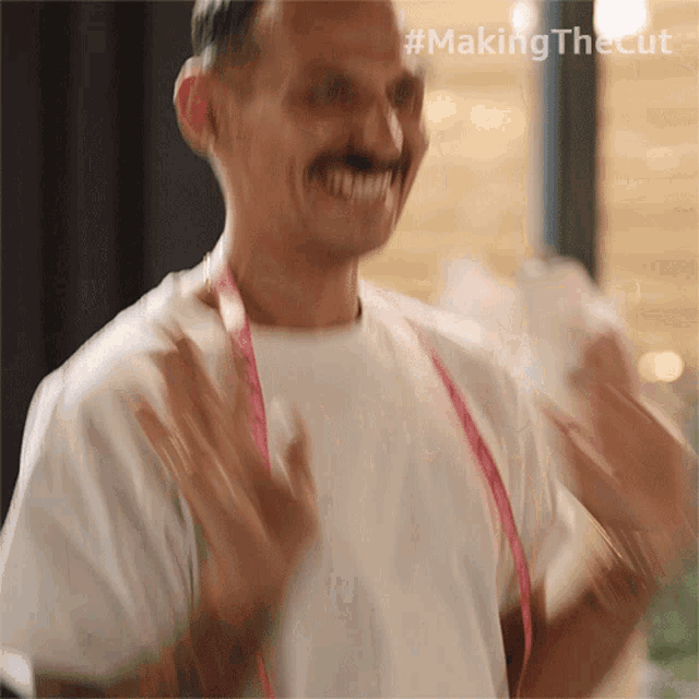 a man wearing a white shirt and a pink measuring tape around his neck has the hashtag #making the cut on his face