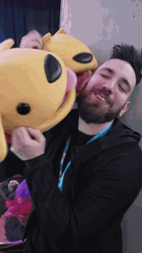 a man with a lanyard around his neck holds a stuffed animal with a pink nose
