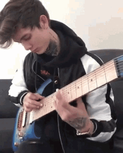 a young man is sitting on a couch playing a blue electric guitar .