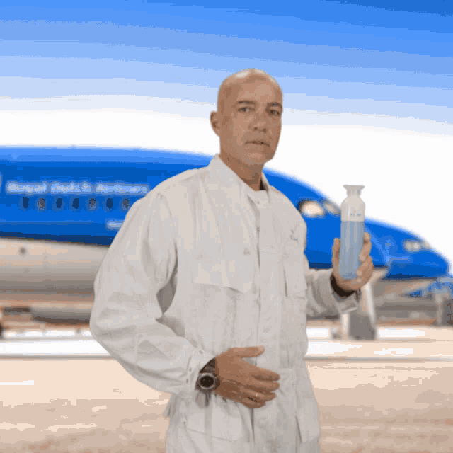 a man is holding a bottle in front of a blue royal dutch airlines plane