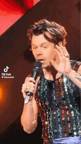 harry styles is holding a microphone and making a funny face on stage .