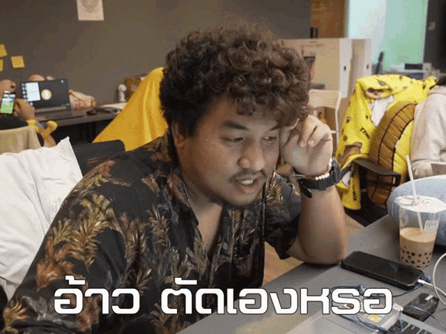 a man with curly hair is sitting at a desk with a cup of coffee and a phone