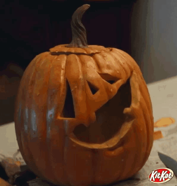 a pumpkin with a face carved into it is on a table next to a kitkat candy bar .