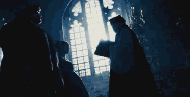 a man and woman are standing in front of a window while a priest stands behind them