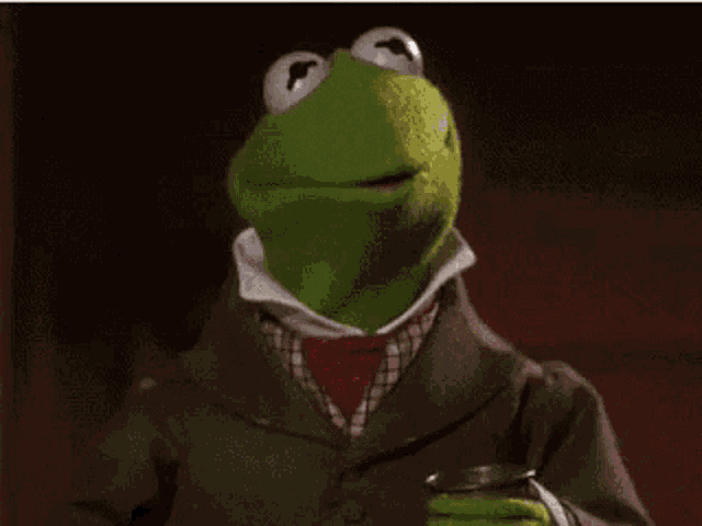 kermit the frog is wearing a suit and tie and holding a cup of tea .