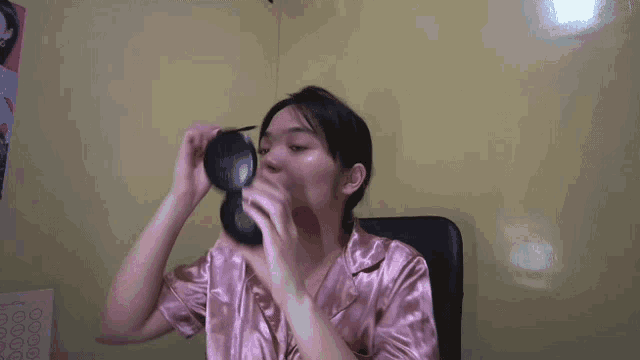 a woman in a pink pajamas is applying makeup to her face in front of a mirror .