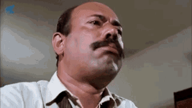 a bald man with a mustache is smoking a cigarette and making a face .