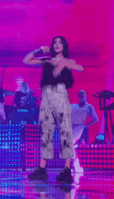 a woman singing into a microphone on a stage with a pink background