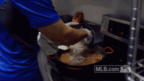 a man in a blue shirt is cooking in a kitchen with a mlb.com logo on the stove
