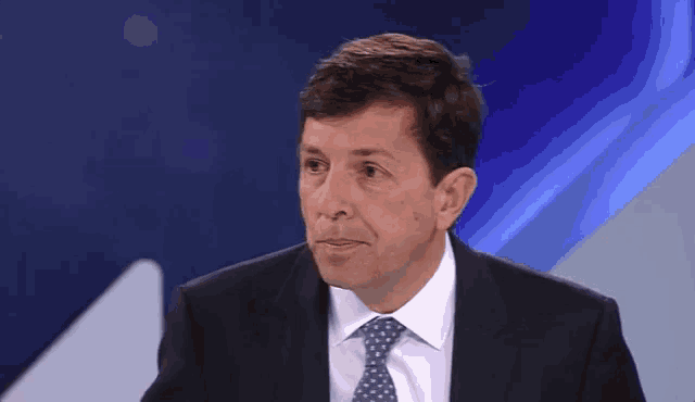 a man in a suit and tie is sitting in front of a blue backdrop