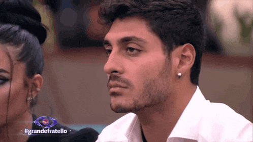a man in a white shirt is sitting next to a woman and a sign that says grandefratello