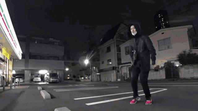 a man in a hooded jacket walking down a street at night