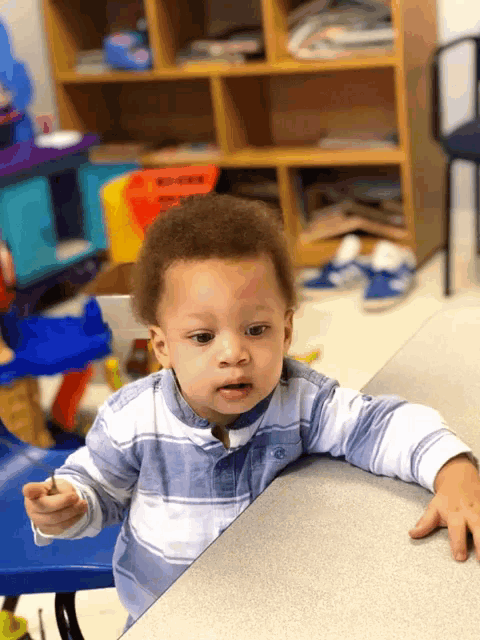 a little boy sitting at a table with a shelf behind him that says " we need "