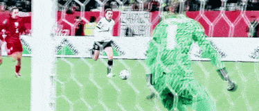 a woman is kicking a soccer ball in front of a goalie with the number 1 on his shirt .