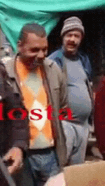 a man with a big belly is standing in front of a sign that says ' tosta ' on it