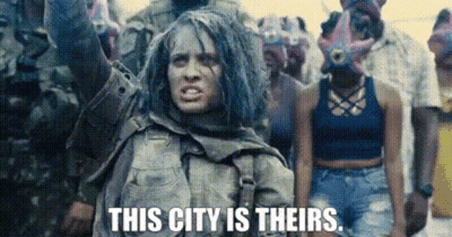 a woman with dreadlocks is standing in front of a crowd of people and says `` this city is theirs ''