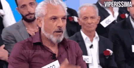 a man with a beard is sitting in front of a crowd of men .