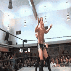 two men are wrestling in a ring with a crowd watching .