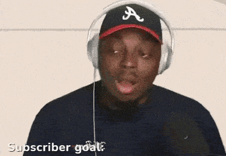 a man wearing headphones and an atlanta braves hat says " subscriber goal "