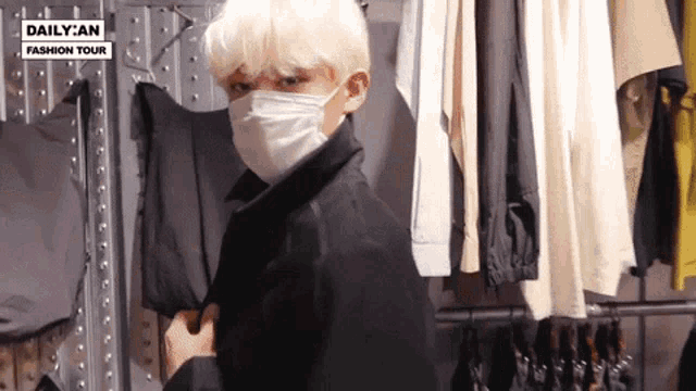 a man wearing a face mask is standing in front of a rack of clothes .