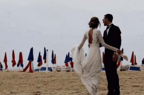 a bride and groom are walking on a beach with umbrellas in the background