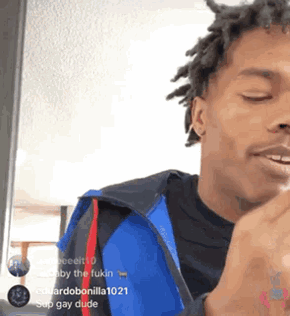 a man with dreadlocks is making a funny face while wearing a blue and black jacket .