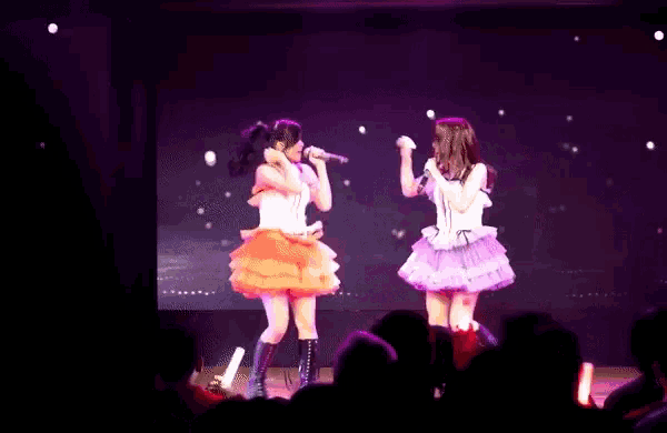 two women are singing on a stage with a crowd watching