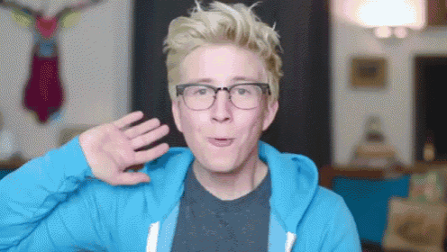 a young man wearing glasses and a blue hoodie waves his hand
