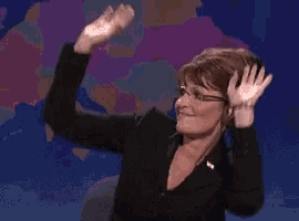 a woman in a black suit and glasses is waving her hands in the air