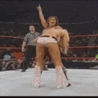 two women are wrestling in a wrestling ring with a referee in the background .