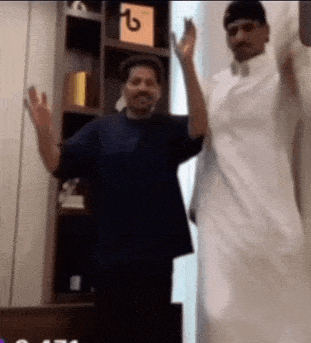 two men are standing next to each other in front of a bookshelf .