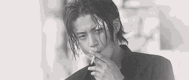 a man with wet hair is smoking a cigarette in a black and white photo .