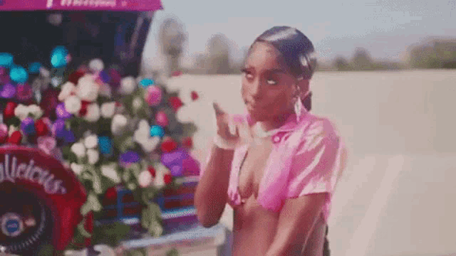 a woman in a pink bikini is blowing a kiss in front of a purple car .