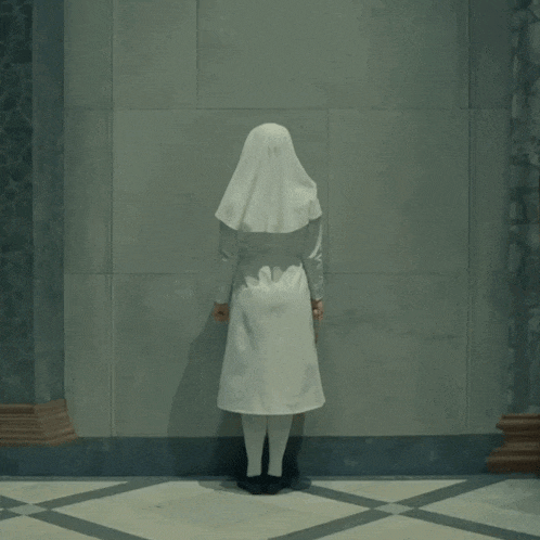 a nun in a white uniform stands in front of a gray wall